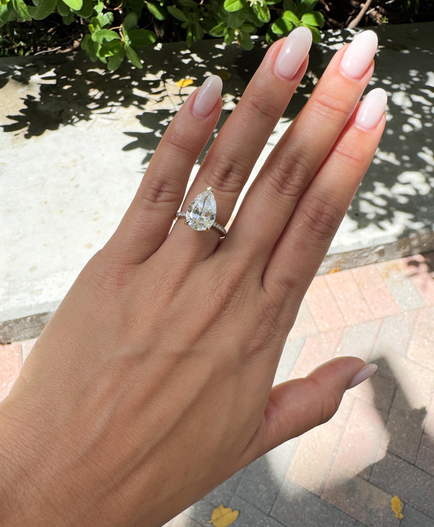 Women's hand wearing a diamond ring with a blurred outdoor background